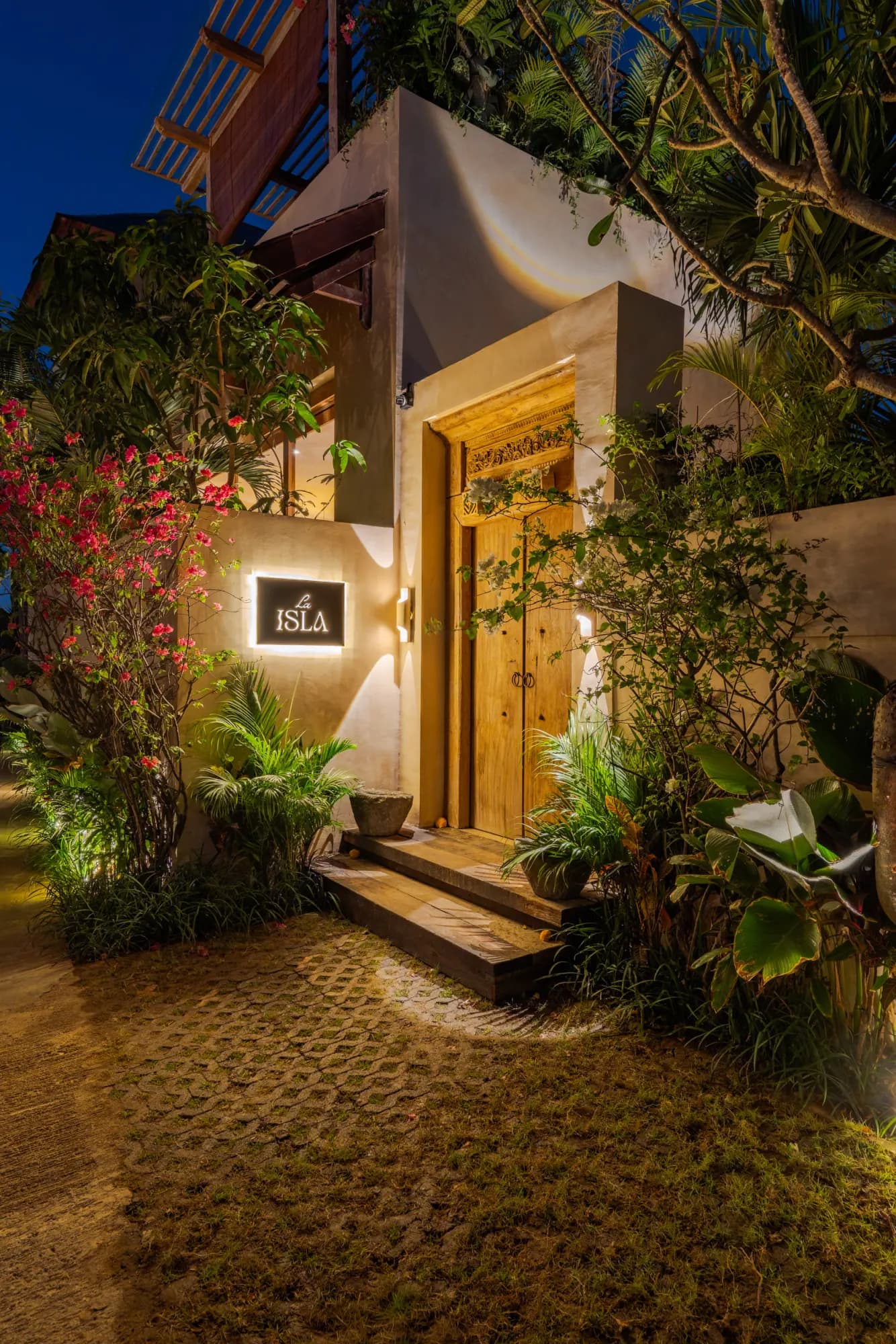 Illuminated entrance gate at night with tropical landscaping