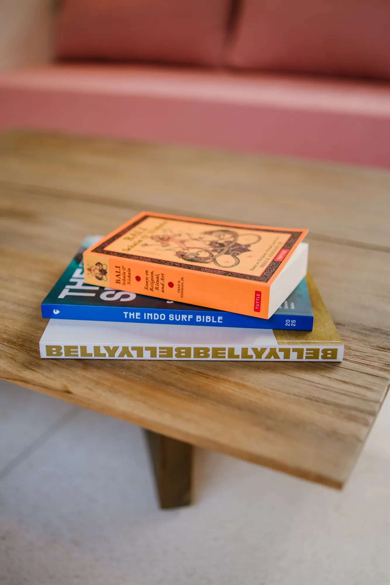 Collection of books arranged on wooden table with coral wall backdrop
